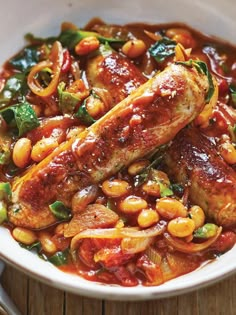 a white bowl filled with meat, beans and veggies on top of a wooden table