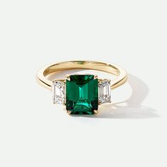 Murphy | 18ct Yellow Gold Created Emerald and Lab Grown Diamond Ring Welcome to the epitome of elegance and sophistication with our Murphy 18ct Yellow Gold Created Emerald and Lab Grown Diamond Ring. This exquisite piece exudes timeless beauty and luxury like no other. Crafted with precision and passion, the Murphy ring boasts a mesmerizing created emerald center stone that radiates brilliance accompanied by two lab-grown diamonds that shimmer with every movement. Metal Height (mm) Width (mm) Certificate 18ct yellow gold 6.5 1.9 Authenticity Certificate Total Carat Weight Colour Clarity Shape 0.58ct G VS2 Emerald Cut Type Colour Dimensions Created Emerald Green 9*7mm Experience the allure of a vintage diamond ring design, symbolizing the past, present, and future. Perfect for marking speci Gold Emerald Cut Emerald Ring, Emerald With Diamonds Ring, Emerald Cut Emerald Ring Gold, Emerald Green Diamond Ring, Emerald Cut Trilogy Ring, Emerald Cut Emerald Engagement Ring, Engagement Rings Emerald Green, Emerald Gold Engagement Ring, Emerald Stone Engagement Ring