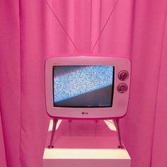 a pink television set sitting on top of a white stand in front of a pink curtain