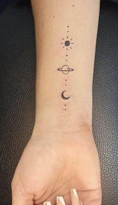 a woman's hand with a small tattoo on the wrist that has planets and stars