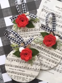 three tags with red roses and green leaves on top of sheet music paper, tied to ribbon