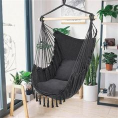 a black hammock chair hanging from a wooden stand in a room with potted plants