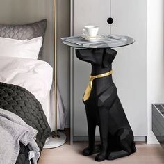 a cat shaped table with a cup on it in the middle of a room next to a bed