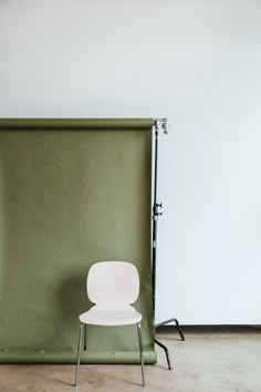 a white chair sitting in front of a green wall with a metal frame on it