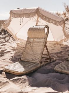 two lawn chairs sitting on top of a sandy beach next to an open white umbrella