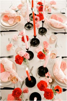 the table is set with pink and red flowers, black candles, and white plates