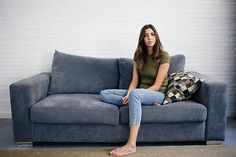 a woman sitting on top of a blue couch in front of a white brick wall