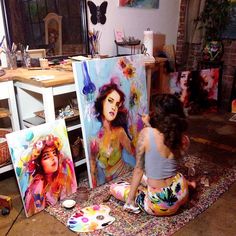 a woman sitting on the floor in front of two canvass that have been painted