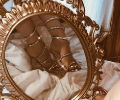 a woman's feet in high heels are reflected in a gold framed mirror on a bed