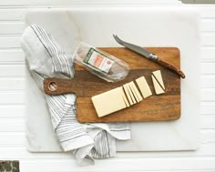 a cutting board topped with cheese next to a knife and some napkins on top of it