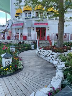 a wooden walkway surrounded by flowers next to a white building with red and yellow doors