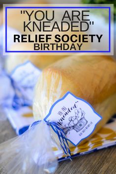 bread wrapped in plastic on top of a wooden table with the words, you are kneaded relief society birthday