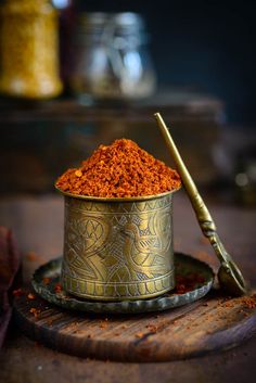 a metal bowl filled with red powder next to a golden spoon on top of a wooden table