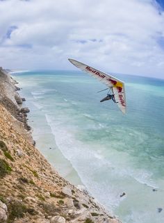 a person flying a kite on top of a cliff next to the ocean and beach