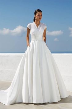 a woman in a white wedding dress standing on the beach with her hand on her hip