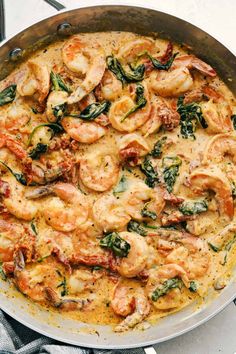 a skillet filled with shrimp and spinach on top of a white tablecloth