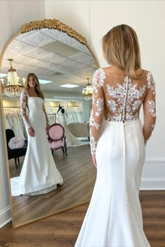 a woman in a white wedding dress looking at herself in the mirror with her back to the camera