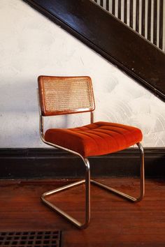 an orange chair sitting in front of a stair case next to a wooden floor and white wall