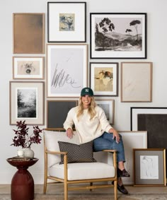 a woman sitting on a chair in front of many framed pictures