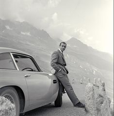 a man leaning on the side of a car in front of some mountains and rocks