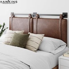 a bed with white sheets and brown headboard, next to a potted plant