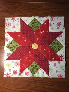 a red and green quilted star on top of a wooden floor with snowflakes