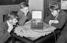 three young boys sitting at a table playing with an old fashioned video game console controller