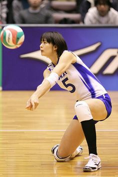 a woman in blue and white uniform playing volleyball on court with spectators watching from bleachers