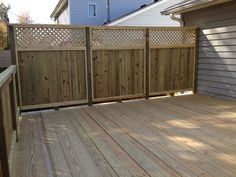 a wooden deck in front of a house next to a garage with a fence on it