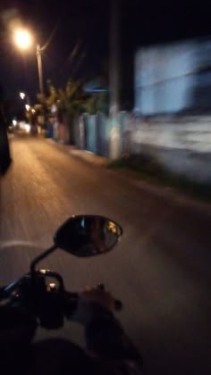 a person riding a motorcycle down a street at night with the headlights on and one hand on the handlebars