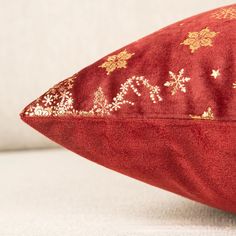 a red pillow with gold stars and snowflakes on the front is sitting on a white surface