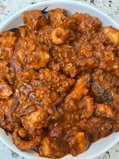 a white bowl filled with meat covered in sauce on top of a marble countertop