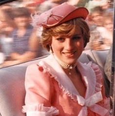 a woman sitting in the back seat of a car wearing a pink dress and hat