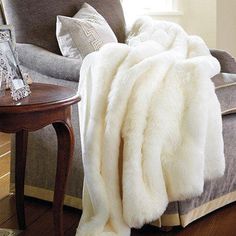 a white fur blanket sitting on top of a couch next to a wooden end table