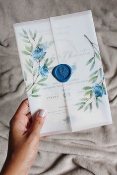 a person holding an open wedding card with blue flowers on it and a wax stamp