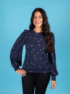 a woman standing in front of a blue background wearing a black top with brown hearts on it