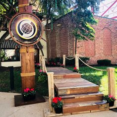 a wooden clock sitting on top of a set of steps next to flowers and trees