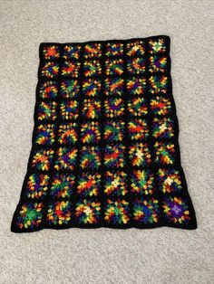 a crocheted black blanket with multicolored flowers on it sitting on the floor