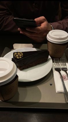 there is a piece of chocolate cake on the table with two cups of coffee next to it