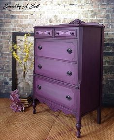 a purple dresser sitting on top of a wooden floor next to a vase with flowers