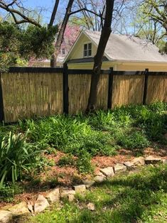 a fence that is next to some grass and rocks in front of a house on a sunny day