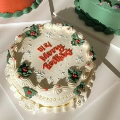 there is a white frosted cake with holly decorations on it and two other cakes in the background