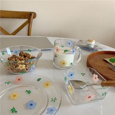 a table topped with plates and bowls filled with food next to a glass bowl full of cereal