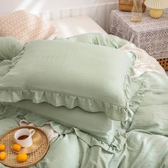 a bed with green sheets and pillows on top of it next to a basket filled with oranges