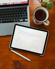 an open laptop computer sitting on top of a wooden desk next to a cup of coffee