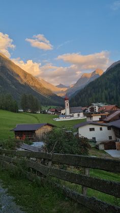 a small village with mountains in the background and a wooden fence around it that leads to a grassy field