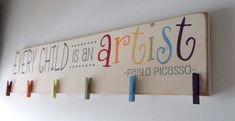 a wooden sign that says every child is an artist and has five pegs attached to it