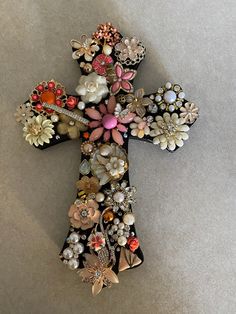 a cross made out of various types of buttons and beads on a table top with a gray background