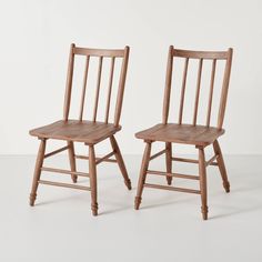 two wooden chairs sitting next to each other on a white surface with one chair missing the seat