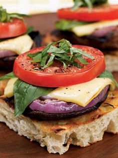 two grilled sandwiches with tomatoes and cheese on a wooden plate next to fresh basil